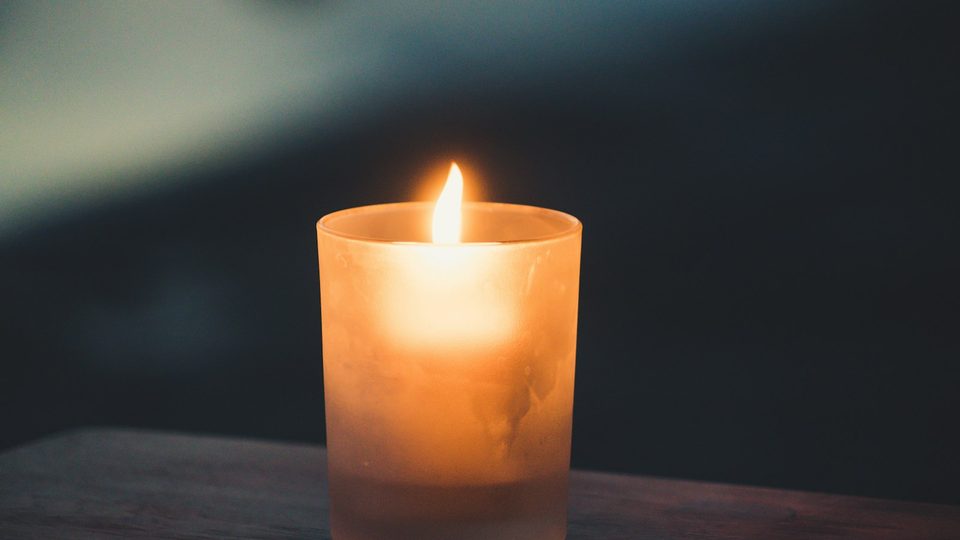 A single lit candle against a dark background.