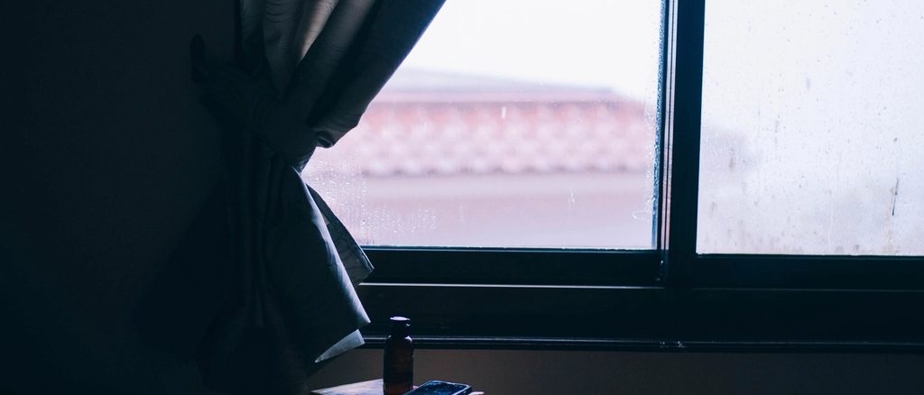 A curtain hanging at a window, backlit by the pale light of an overcast morning.