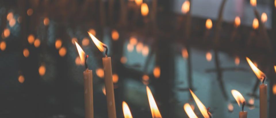 Rows of lit candles in a church, their flames small against the dark.