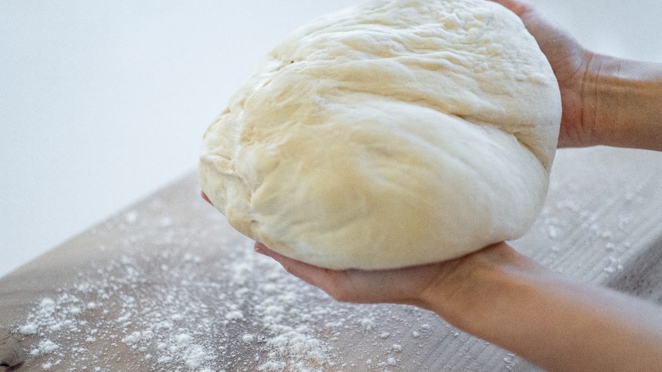 Two hands cradling a round of dough on a floured worktop, ready to be shaped.